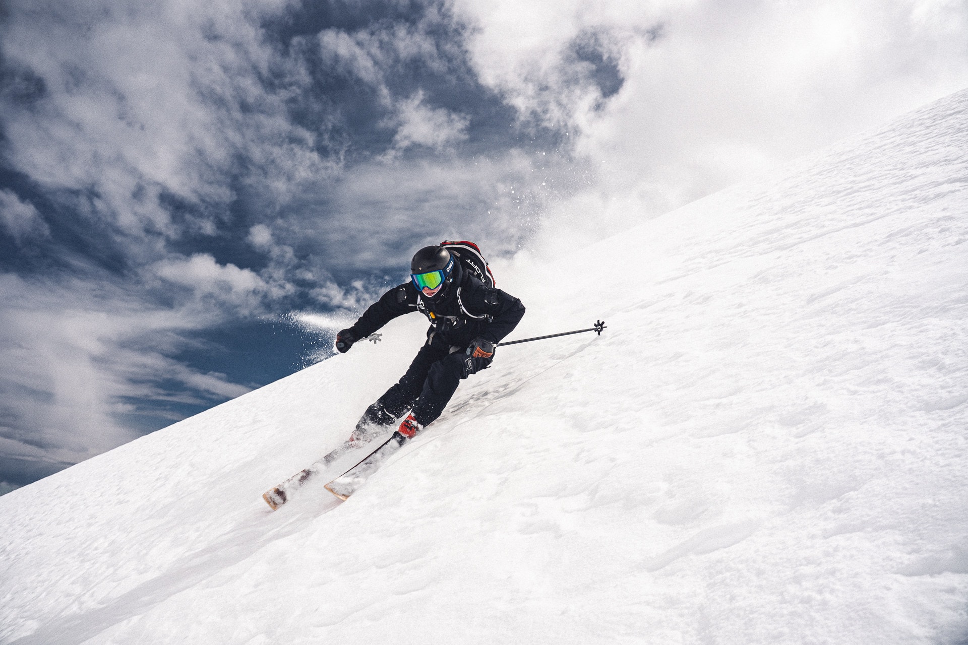 A skier carving hard down a steep face under a cloudy sky
